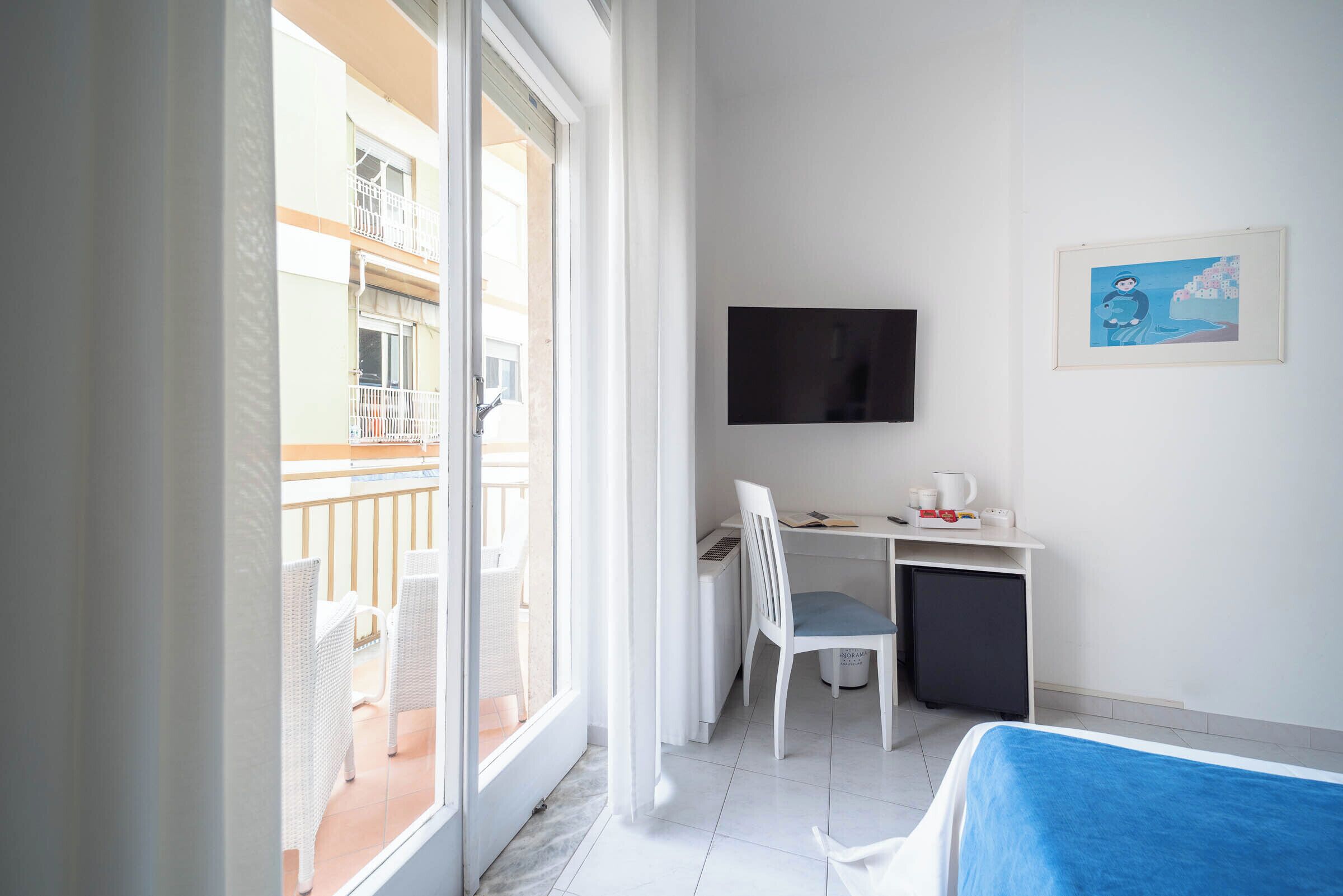 A hotel room with a balcony, a desk with a chair, a TV, and a bed.