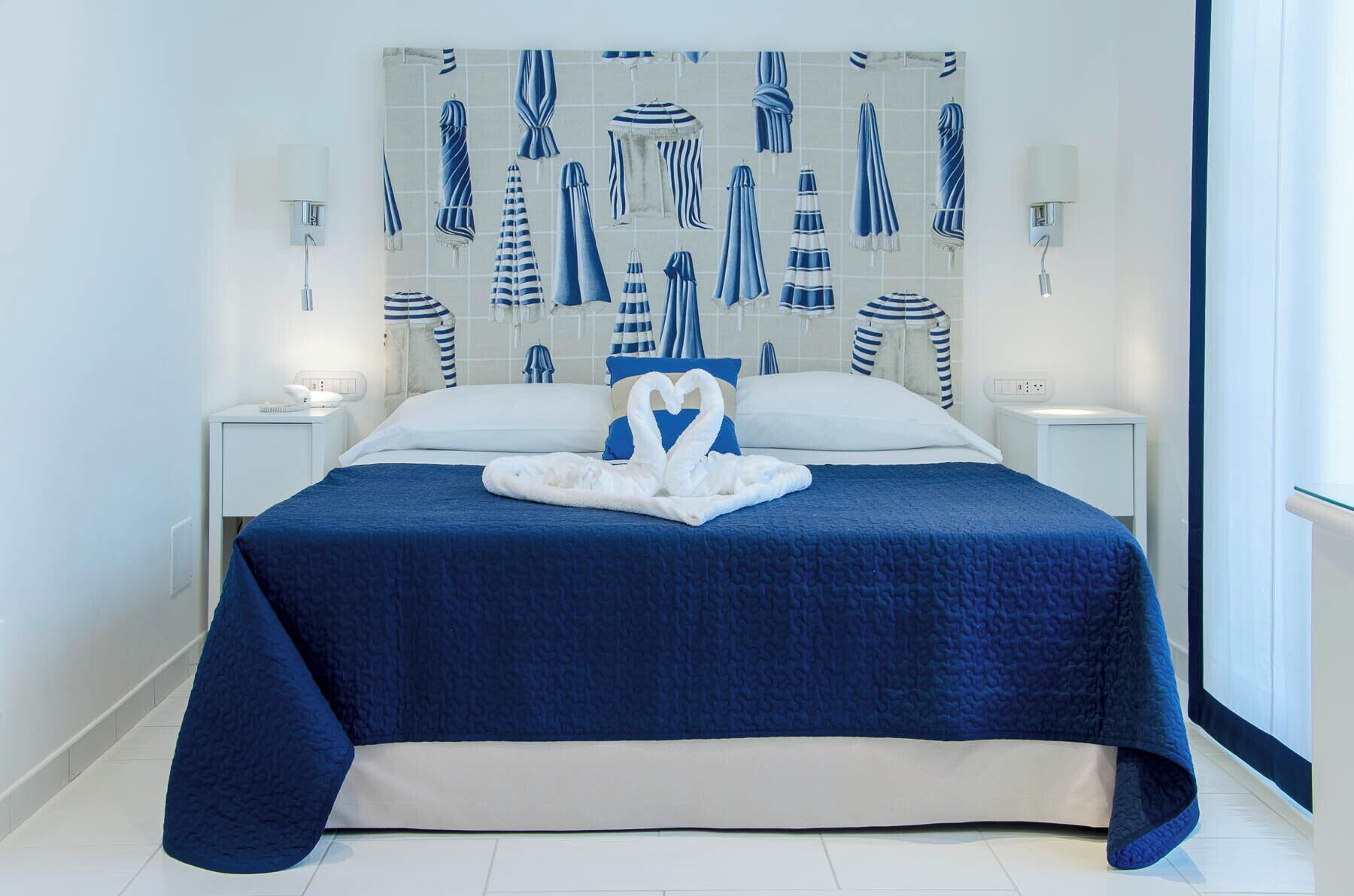 A hotel room with a large bed, a heart-shaped towel arrangement, and a wall decorated with towels.