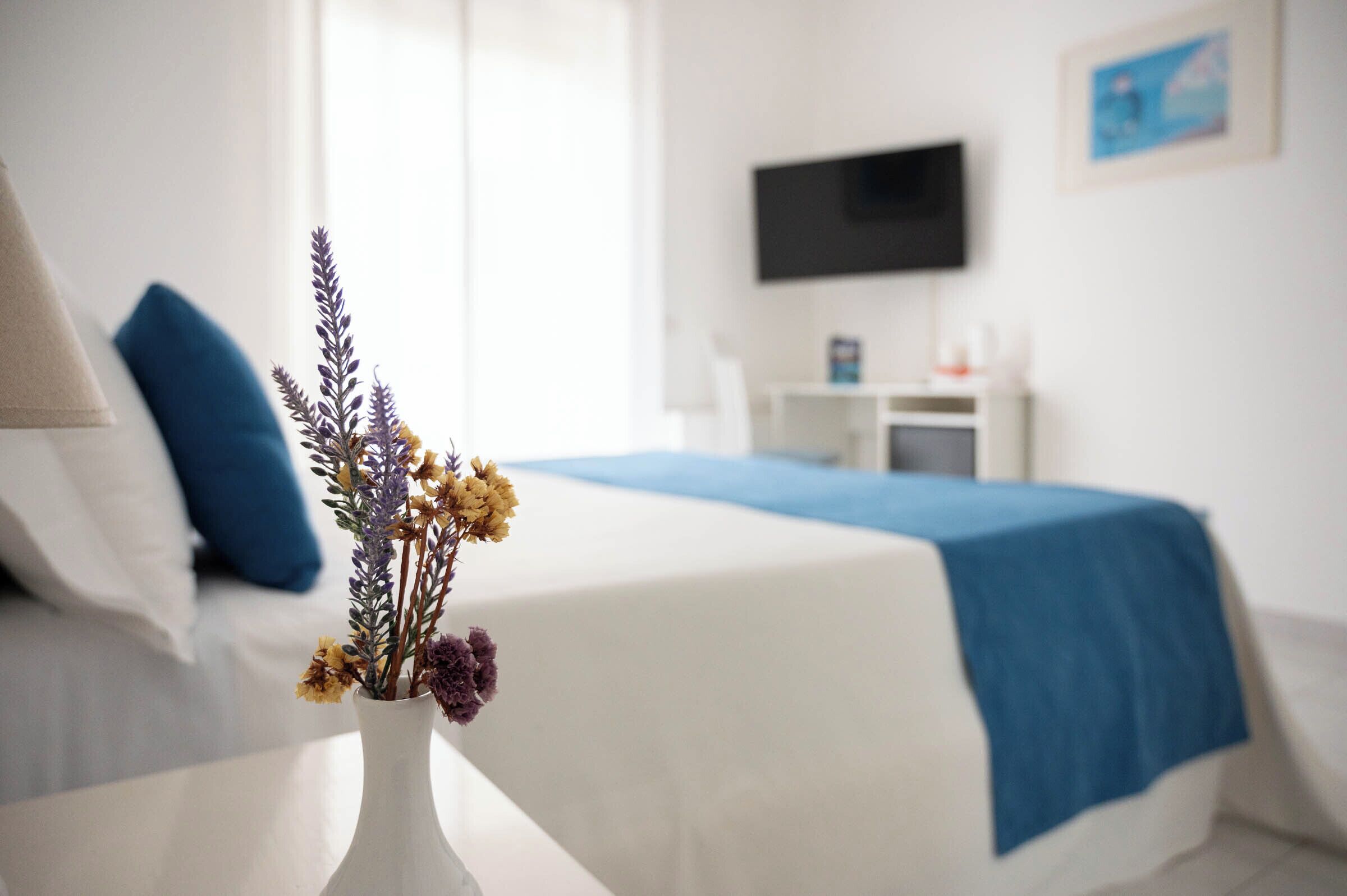 Habitación de hotel con cama, escritorio, televisor y un florero con flores.