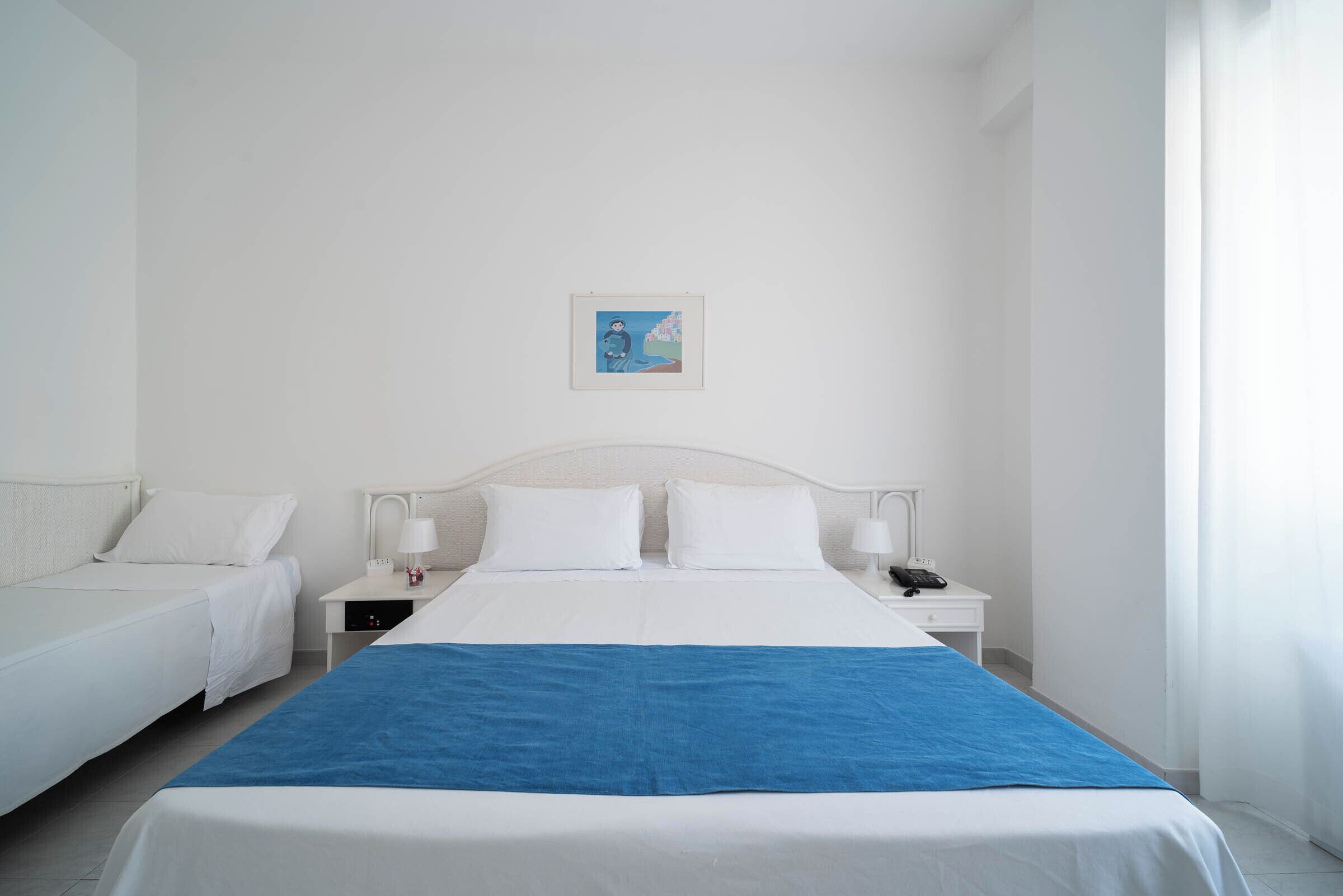 A hotel room with a large bed, two bedside tables with lamps, a small bedside table with a phone, and a framed picture on the wall.