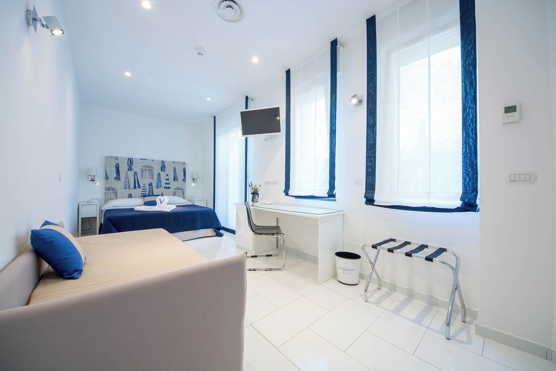 A modern hotel room with a bed, a desk, a chair, and a radiator.