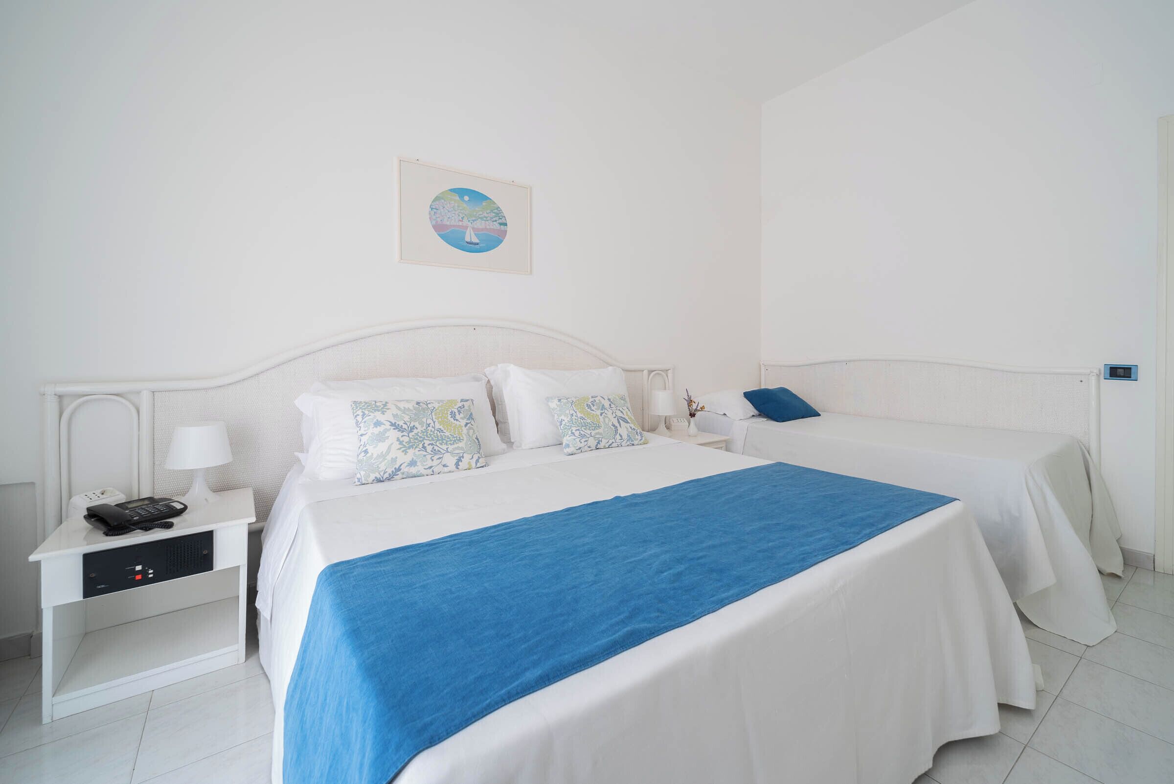 Habitación de hotel con una cama grande, otra más pequeña, una mesita de noche con un teléfono y un cuadro en la pared.