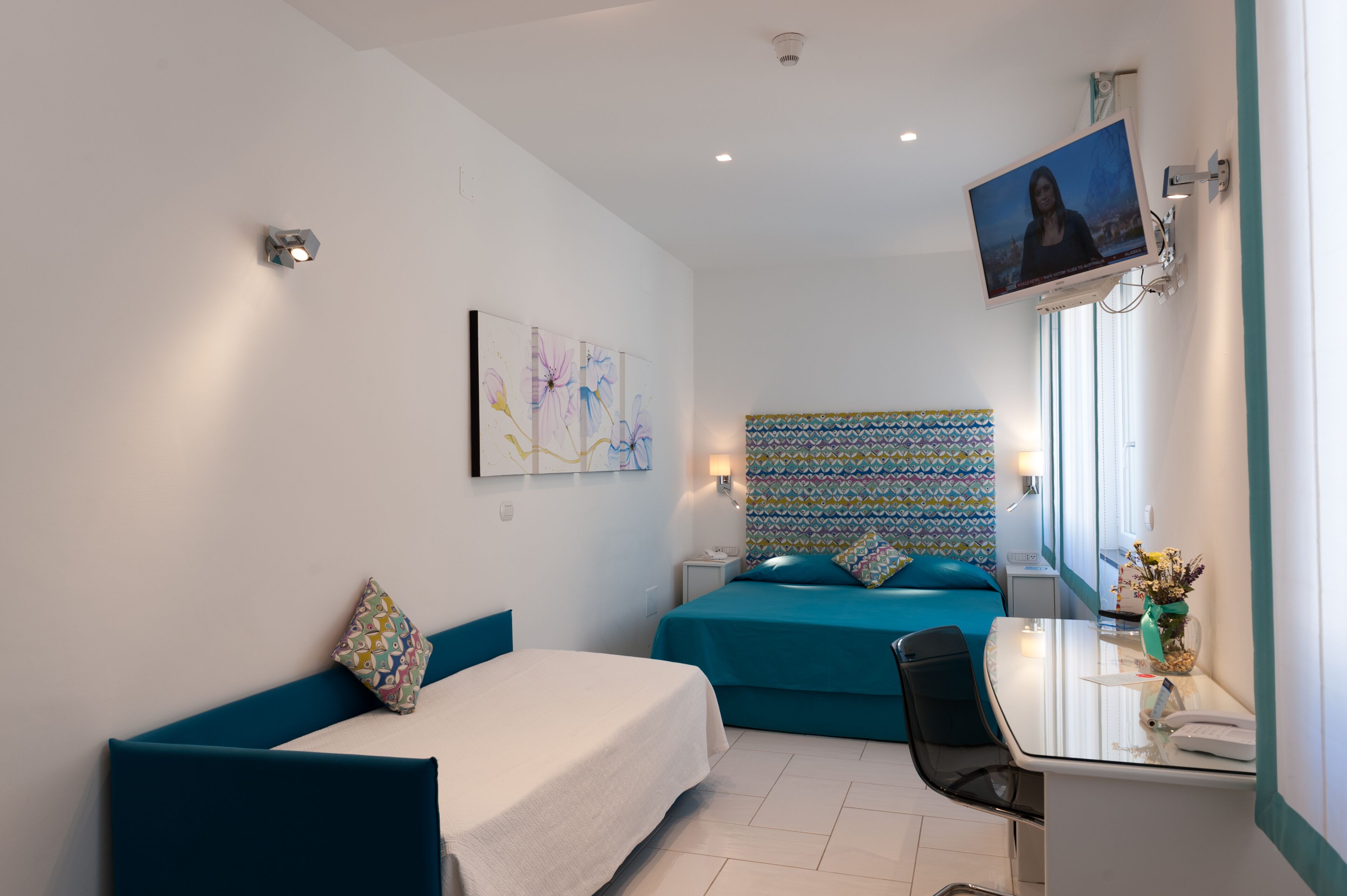A hotel room with two beds, a desk with a chair, a TV mounted on the wall, and a window with a view.