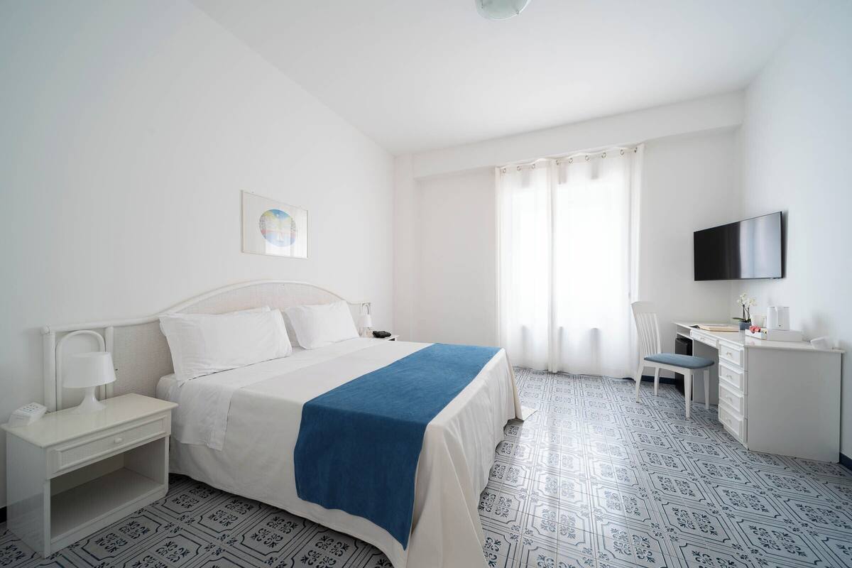 Ein Hotelzimmer mit Bett, Schreibtisch, Stuhl, Fernseher und einem Fenster mit Vorhängen.