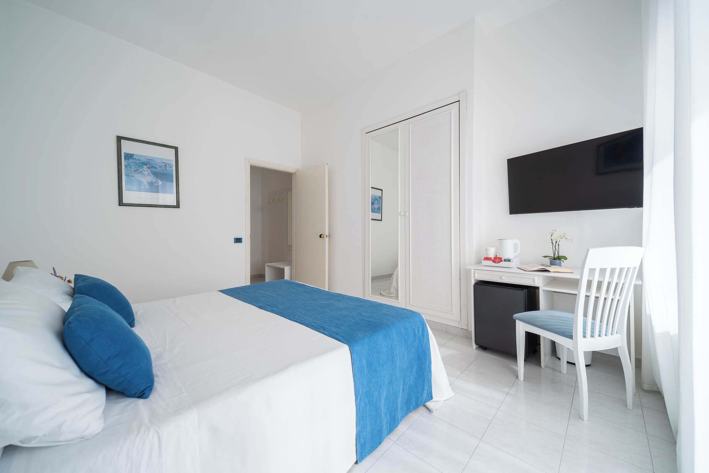 A hotel room with a bed, a desk, a chair, a TV, and a small fridge.