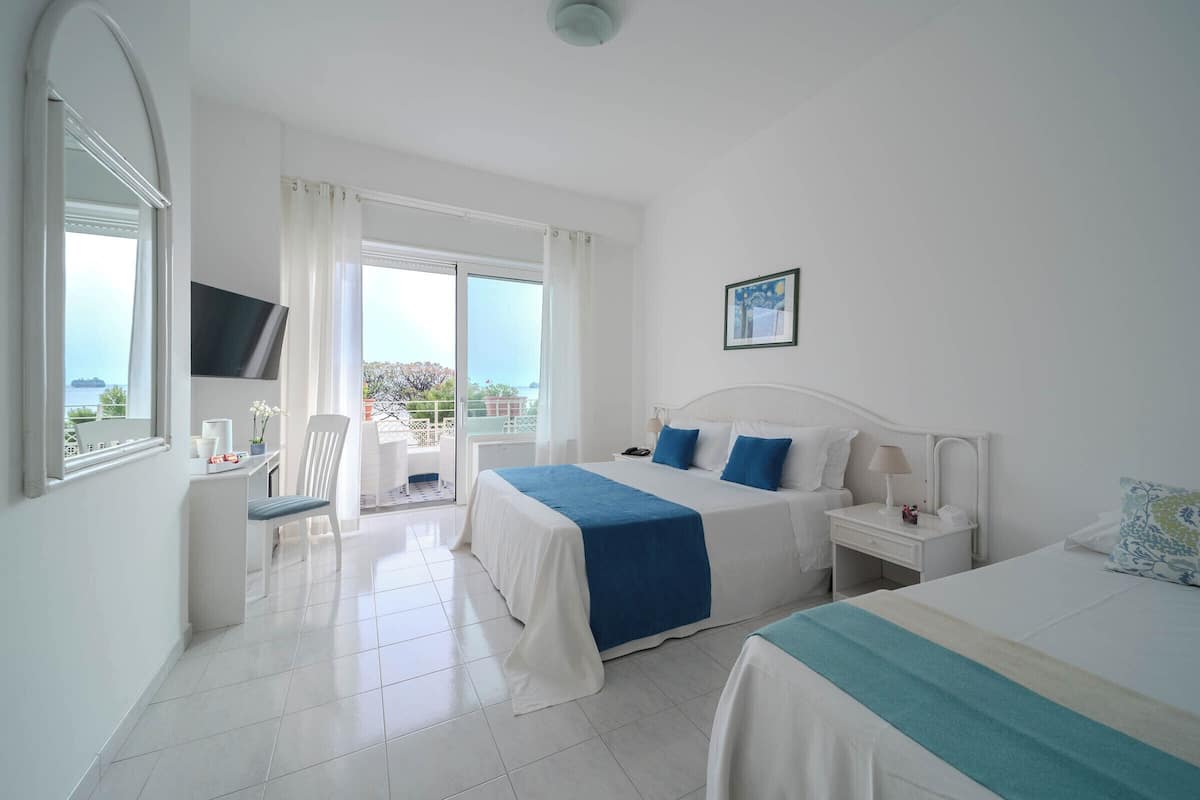 Ein Hotelzimmer mit zwei Betten, einem Fernseher, einem Balkon und Meerblick.