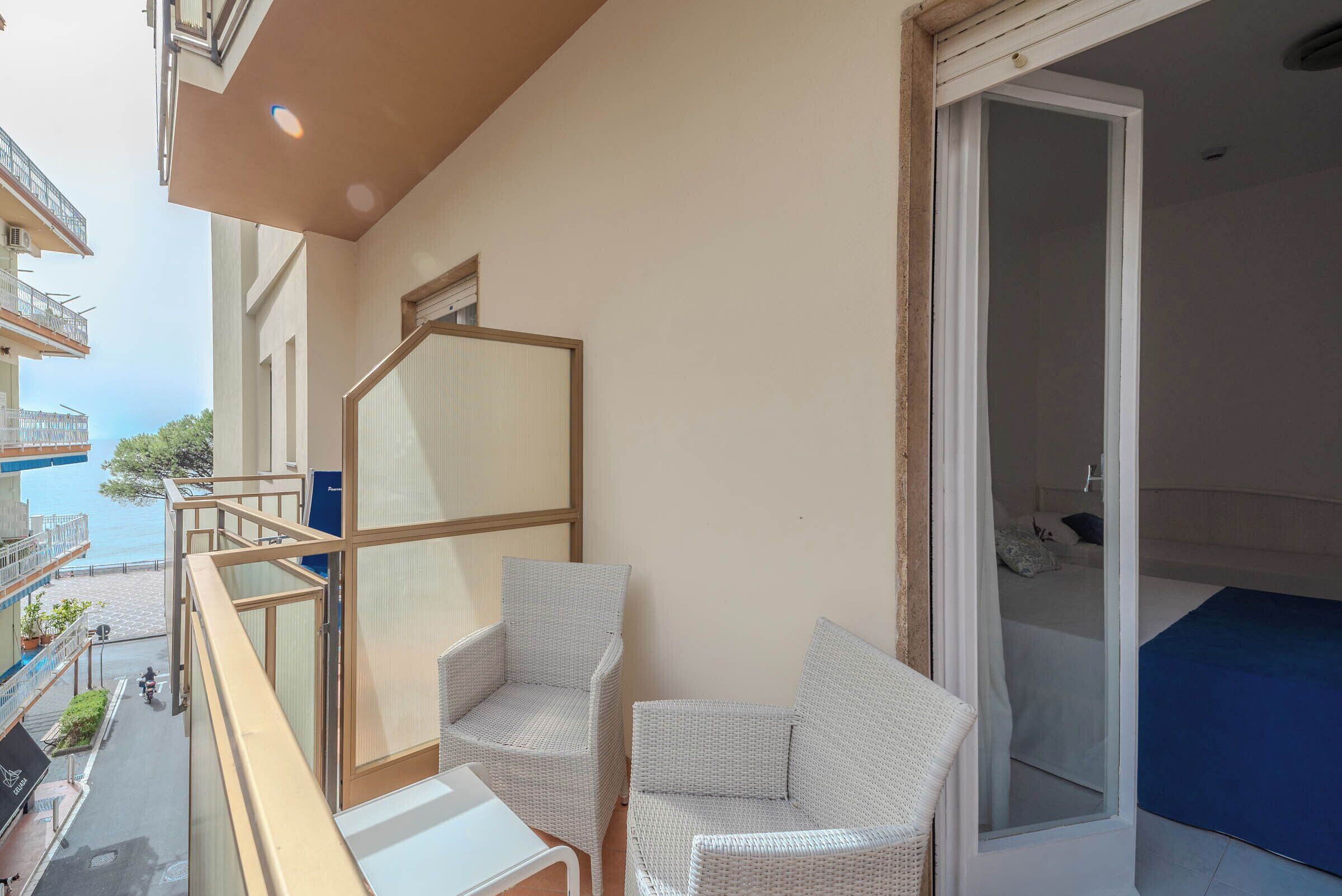 A balcony with two wicker chairs, a small table, and a view of the sea.