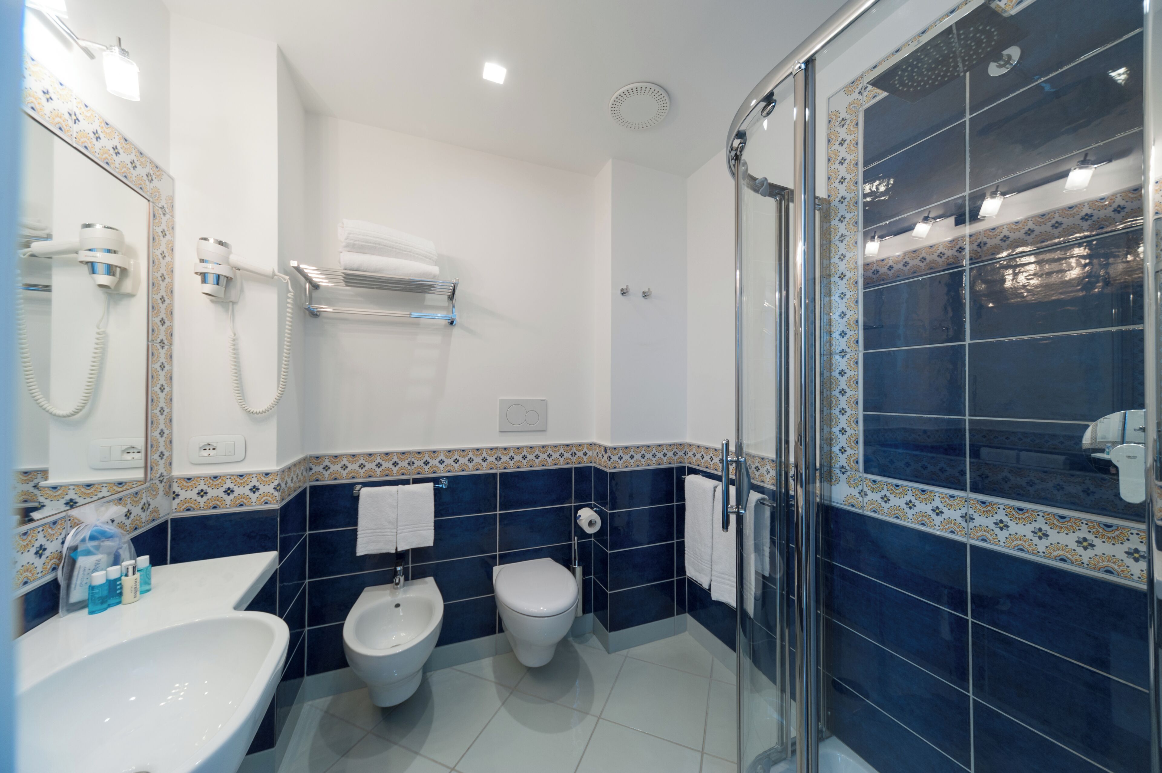 Un baño moderno con cabina de ducha de vidrio, un bidé, un inodoro y un lavamanos con espejo.