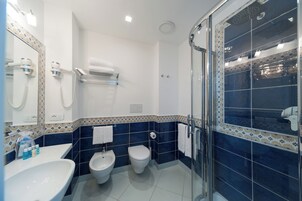 Un baño moderno con cabina de ducha de vidrio, un bidé, un inodoro y un lavamanos con espejo.