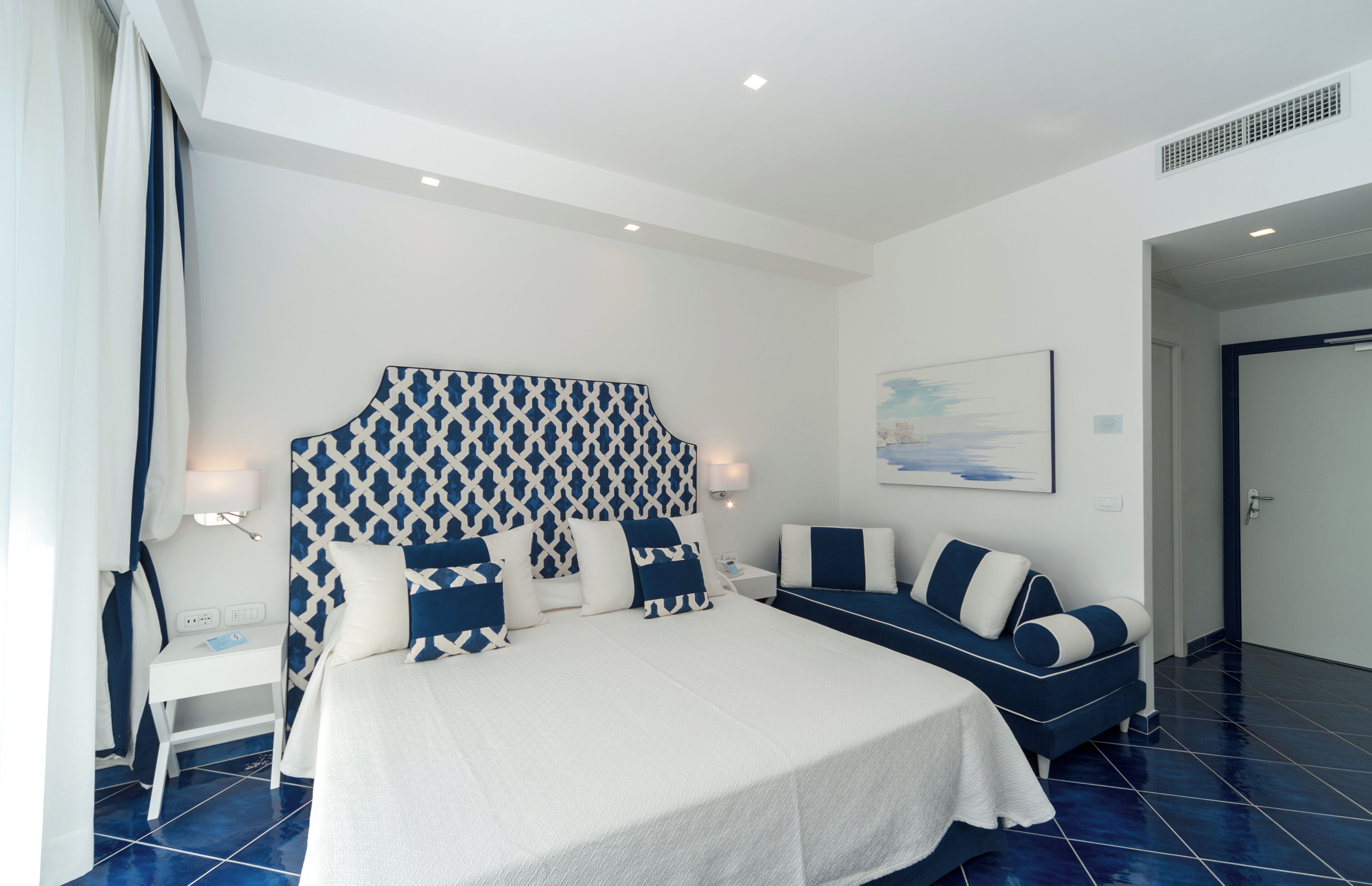 Una habitación de hotel moderna con una cama grande, un sofá, una mesita de noche y un cabecero montado en la pared.