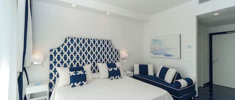 Una habitación de hotel moderna con una cama grande, un sofá, una mesita de noche y un cabecero montado en la pared.
