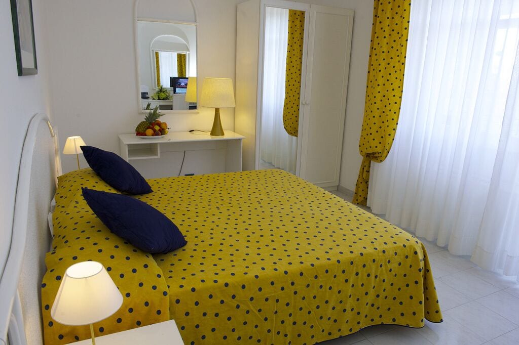Une chambre à coucher avec un lit, des lampes de chevet, un bureau avec un miroir et un panier de fruits.