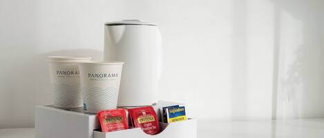 Una cafetera blanca, dos tazas y una bandeja con sobres de té y café.