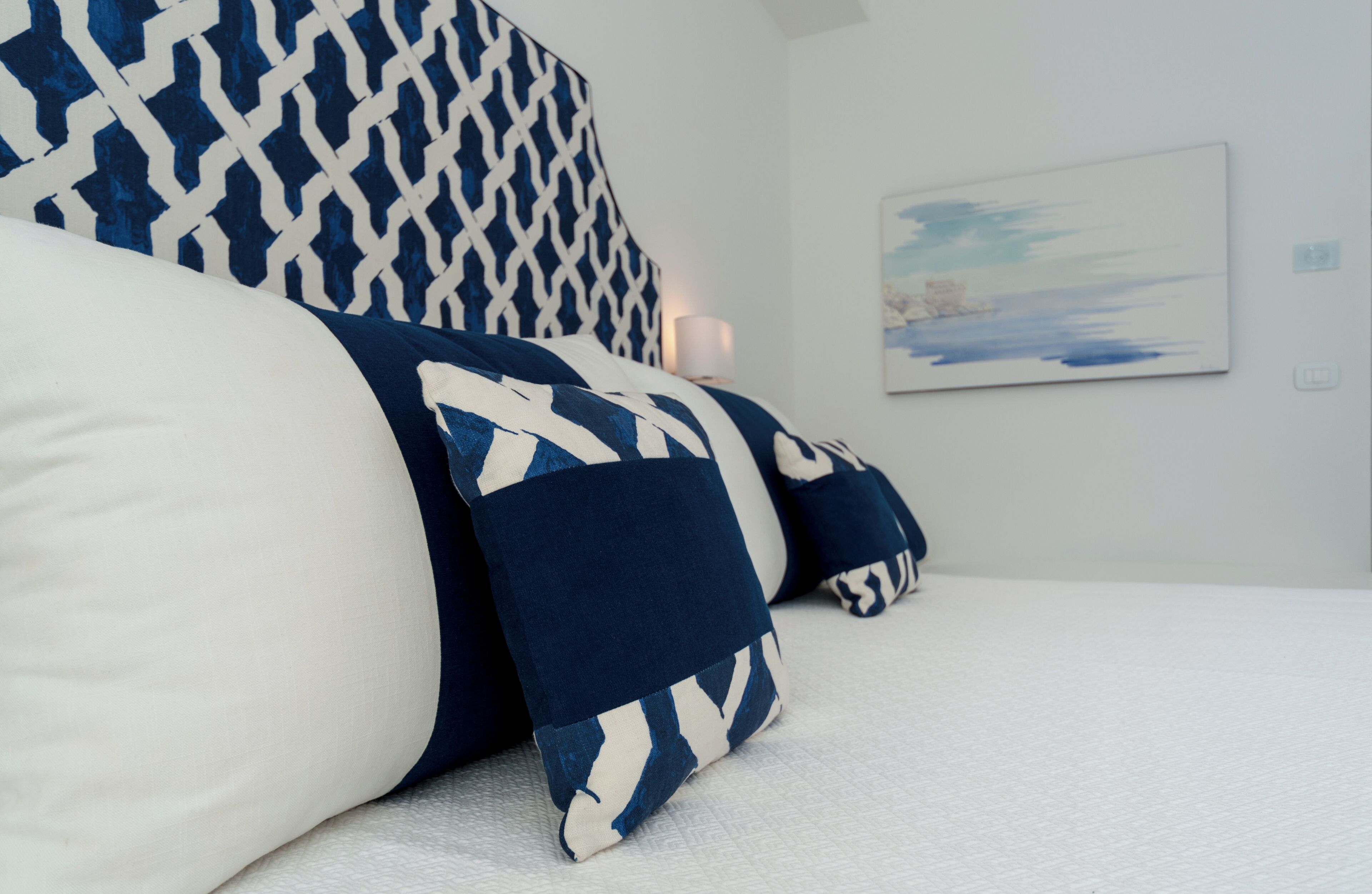 A bed with patterned pillows and a painting on the wall.