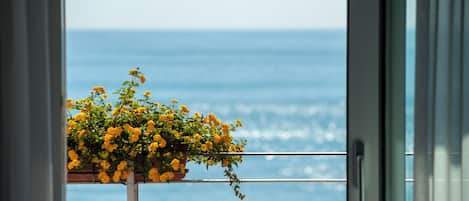 A balcony with a view of the sea, a potted plant with yellow flowers, and a white railing.