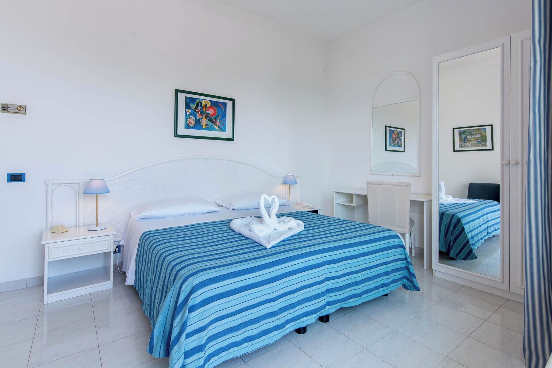 A hotel room with a bed, two bedside tables with lamps, a dresser, a mirror, and a door.