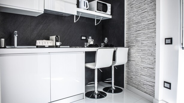 Een moderne keuken met witte kasten, een magnetron en twee barkrukken.