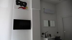 Een kamer met een flatscreen televisie, een bureau met stoel, een spiegel en een wandairconditioner.
