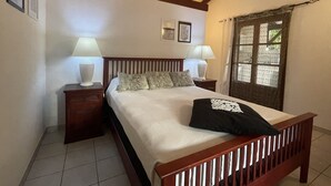 Une chambre avec un lit en bois, deux tables de chevet avec des lampes, une fenêtre donnant sur un beau paysage et un plafond avec des poutres apparentes.
