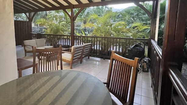 Un espace extérieur aménagé en terrasse, avec une table ronde et des chaises, des rampes en bois et une vue sur la végétation tropicale.