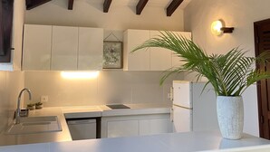 Une cuisine avec des meubles blancs, un plan de travail blanc, un évier, une cuisinière et une plante en pot.