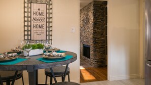 Un coin repas avec une table ronde dressée pour quatre personnes, une enseigne décorative au-dessus et une cheminée en pierre en arrière-plan.