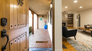Une porte en bois avec une poignée en métal, un pot de fleurs bleu, une chaise noire, une table en bois et une cheminée en pierre.