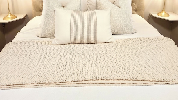 A neatly made bed with a tufted headboard, multiple pillows, and a textured blanket. There are two bedside lamps on either side of the bed.