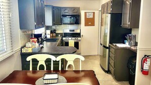 A kitchen with a dining table, chairs, a chandelier, cabinets, a microwave, a stove, and a refrigerator.