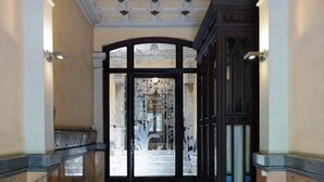 Ein Korridor mit Schachbrettfußboden, einer Glastür mit Strukturmuster und einer dekorativen Decke mit geometrischen Mustern.