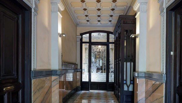 Eine prachtvolle Diele mit Marmorböden, einer verzierten Decke und einer großen Glasdoor, die zu einem Balkon führt.