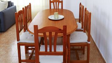 A wooden dining table with six chairs, a white plate with a candle, and a grey sofa in the background.