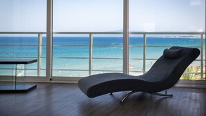 Une chambre moderne dotée d’une grande fenêtre donnant sur une plage, d’un fauteuil et d’une petite table.