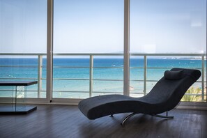 Una habitación moderna con un amplio ventanal con vistas a la playa, una silla de descanso y una pequeña mesa.