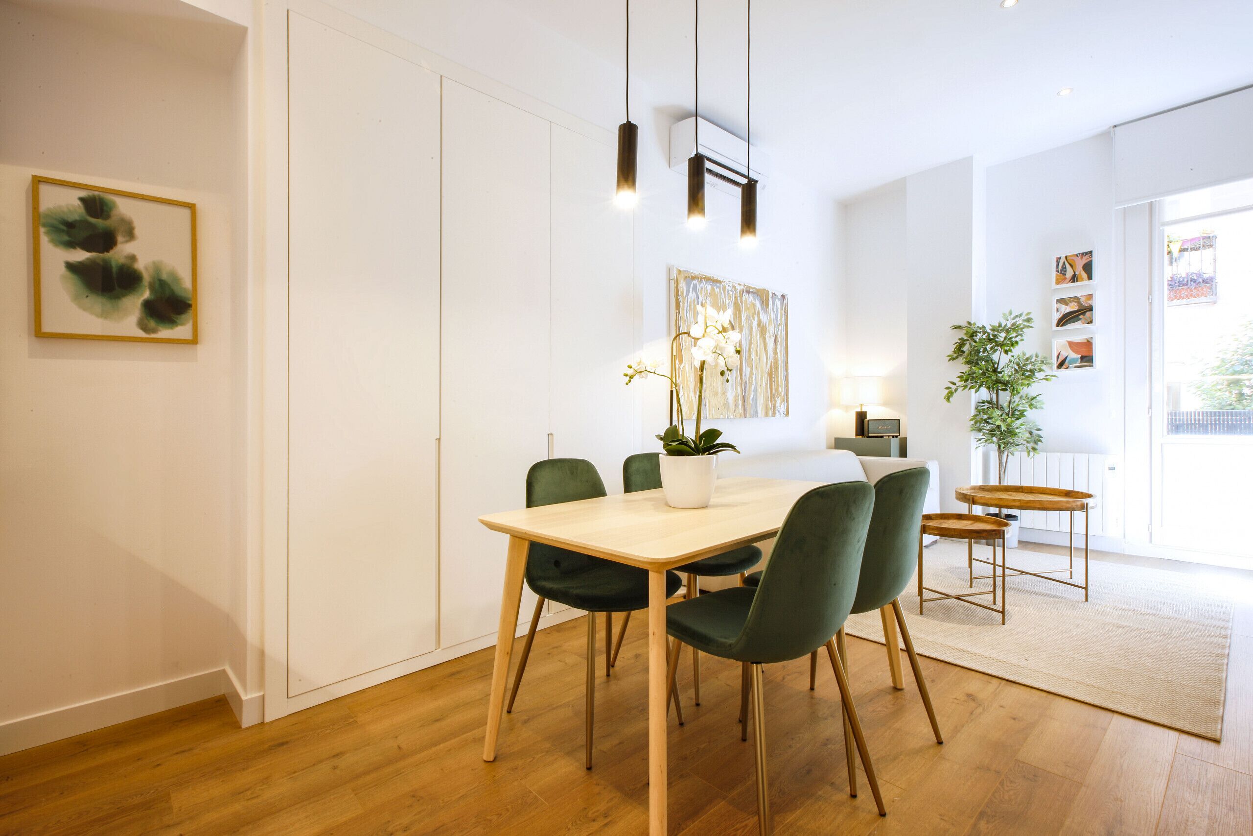 A dining area with a wooden table, green chairs, a potted plant, and artwork on the walls.