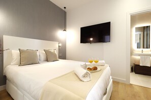 Ein Hotelzimmer mit einem großen Bett, einem flachbildfernseher an der Wand und einem Frühstücksbrett mit Croissants und Orangensaft.