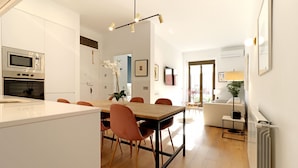 A modern kitchen with a central island, dining area with chairs, and a living space with a sofa and lamp.