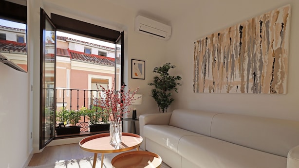A modern living room with a white sofa, a round wooden coffee table, and a potted plant.