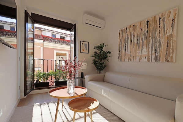Una sala de estar moderna con un sofá blanco, una mesa de centro redonda de madera y una planta en maceta.