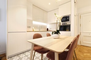 A modern kitchen with white cabinets, a wooden dining table, and a potted orchid. - Royal Madrid (Madrid)