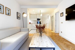 A modern living room with a white sofa, a wooden coffee table with a vase, and a TV mounted on the wall.
