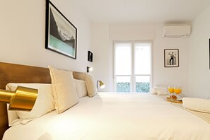 A hotel room with a large bed, a headboard, a window with a view, a wall-mounted air conditioner, and a framed picture on the wall. - Royal Madrid (Madrid)