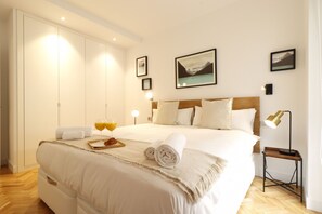 A neatly made bed with a tray of orange juice and towels, a bedside lamp, and framed pictures on the wall.