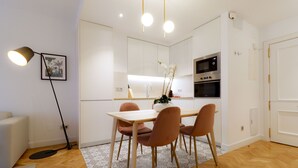 A modern kitchen with white cabinets, a dining table with four chairs, and a black oven.