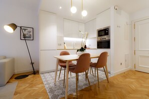 A modern kitchen with white cabinets, a dining table with four chairs, and a black oven.