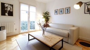A modern living room with a sofa, a coffee table, and a window with a view of trees.