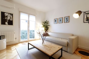 A modern living room with a sofa, a coffee table, and a window with a view of trees.