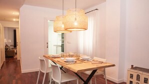 A dining area with a wooden table, white chairs, and wicker pendant lights. - Casa Centro Torrevieja San Policarpo (Torrevieja)