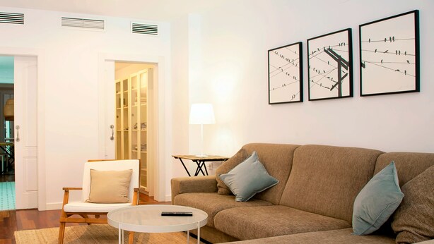A living room with a brown sofa, a white armchair, a small round table, and a lamp. There are three framed pictures on the wall. - Casa Centro Torrevieja San Policarpo (Torrevieja)