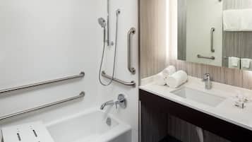 A modern bathroom with a white bathtub, a sink with a mirror, and handrails.